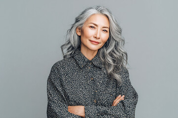 Gray portrait. Silver hair frames mature Asian woman smiling, arms crossed. For lifestyle brand, product shot, health wellness, or corporate headshot.