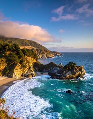 Dramatic coastal scenery unfolds with a tranquil beach, rocky outcrops, and a vibrant turquoise sea, bathed in the warm hues of a golden sunset.