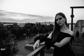 Portrait of a beautiful young woman in a black dress in a city park. Black and white photo.