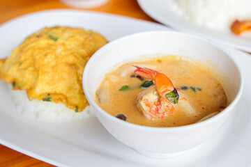 Flavorful Feast: A delectable dish showcases a vibrant shrimp curry served in a white bowl, accompanied by a side of fluffy rice and a golden omelet, presented on a clean white plate.