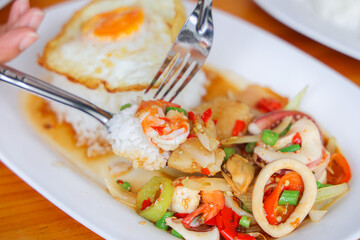 Delectable Seafood Delight: A culinary masterpiece featuring a vibrant medley of seafood with a golden-yolked fried egg and fluffy rice, inviting viewers to savor the delicious experience.