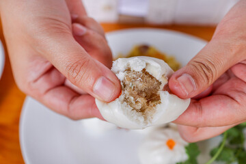 Steamed Bun: A close-up shot of hands tenderly breaking open a succulent steamed bun, revealing its...