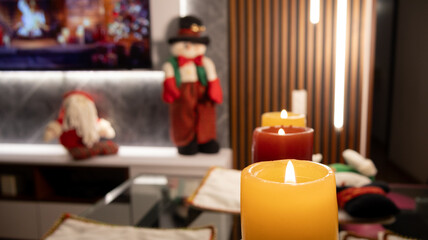 Close-up of glowing Christmas candles in red and yellow on creative glass holders with festive ornaments, creating a warm and cozy holiday atmosphere.