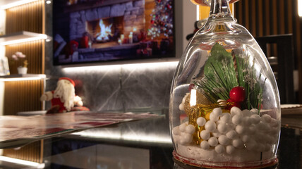 Creative Christmas centerpiece with an upside-down wine glass filled with snow, greenery, berries,...