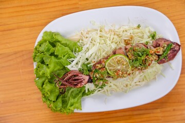 Grilled Squid Dish: A top-down view of a culinary masterpiece, featuring a perfectly grilled squid, adorned with vibrant toppings, beautifully arranged with fresh greens on a stylish plate.