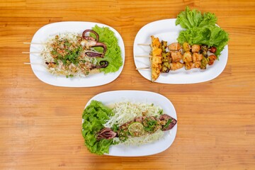 Exquisite Culinary Delights: An overhead shot of three plates of food displays a vibrant composition, featuring skewers of marinated protein and rice.