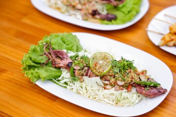 Grilled Squid with Lime: A close-up shot of a grilled squid dish garnished with lime slice and other ingredients on a plate, presenting a delectable culinary creation.