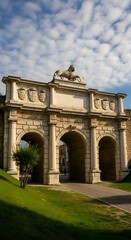 Obraz premium ​A stone triumphal arch with a lion statue on top, set against a blue, cloudy sky