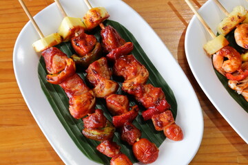 Grilled Delight: A mouthwatering display of grilled meat skewers and pineapple, artfully arranged on a bed of fresh green leaves, evoking feelings of culinary pleasure.
