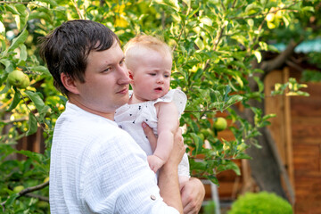 Obraz premium A father gently holds his curious infant beside sunlit apple branches in the backyard orchard, capturing a quiet moment of care and observation