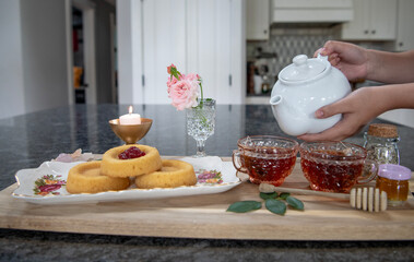 Pouring tea into tea cups at afternoon tea time in bright kitchen. 
