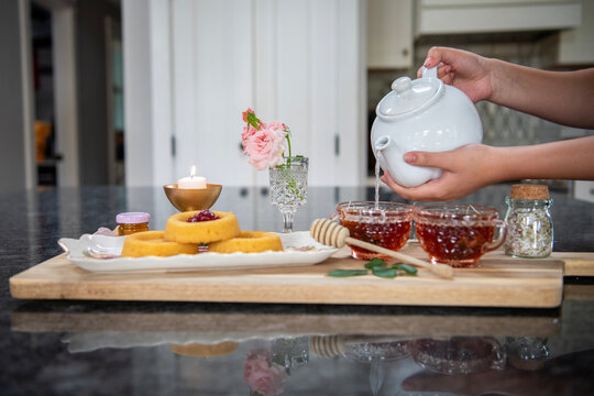 A woman pours hot water from a tea pot into tea cups so  the tea can brew in a lovely, cute, feminine tea party scene.  - Powered by Adobe