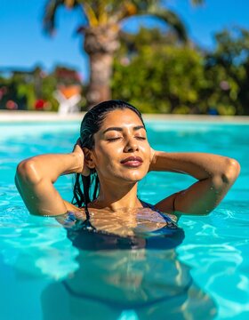 A woman floats peacefully in a turquoise pool, her hands resting on her head. The bright sunny day casts a warm glow, creating a serene outdoor atmosphere.