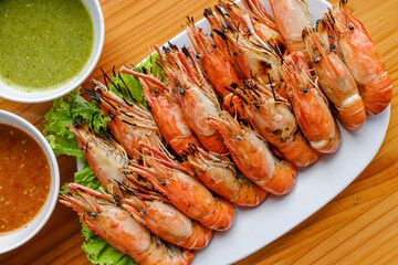Grilled Shrimp Feast: A close-up view showcases a delectable platter of grilled shrimp, meticulously arranged on a bed of fresh lettuce, with vibrant dipping sauces nearby.