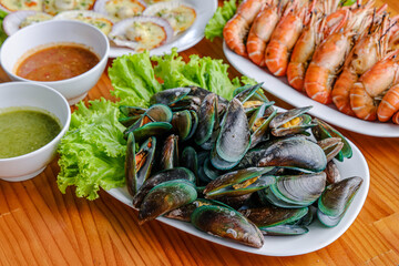 Seafood Platter: An appetizing seafood assortment, featuring a variety of shellfish and prawns, elegantly arranged on a wooden table, accompanied by flavorful sauces and fresh garnishes.