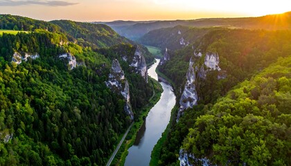 Fototapeta premium Aerial view of a deep valley, a river flowing between cliffs, lush greenery on either side, the sun setting