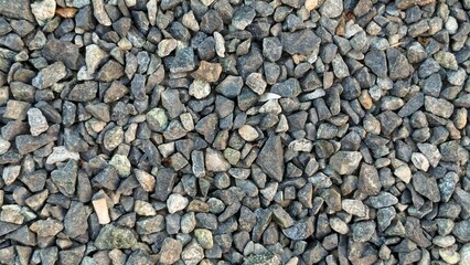 A close-up of small, rough gravel stones in varying shades of gray and tan, filling the frame.