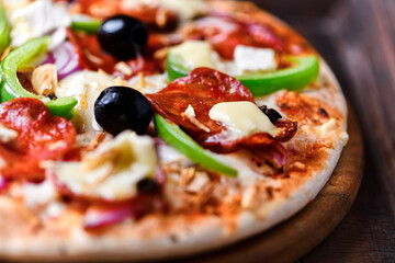 Pizza with chorizo ​​sausage, mozzarella cheese, green pepper and black olives. Rustic wooden background. Soft focus.	