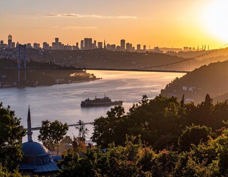 Golden sunrise over a city and river.  A tranquil scene of a bustling metropolis at dawn, with a ferry crossing the waterway, a suspension 
