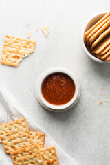 overhead view of tomato sauce in a white ramekin, top view of tomato sauce and crackers on white countertop