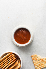 overhead view of tomato sauce in a white ramekin, top view of tomato sauce and crackers on white countertop