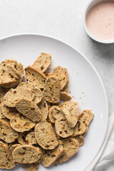 overhead view of slices of savory biscotti and dip, top view of thinly sliced bread chips with sauce, top view of crostini bread slices on marble countertop