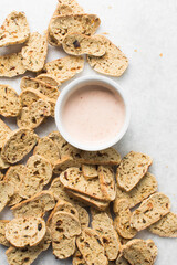 overhead view of slices of savory biscotti and dip, top view of thinly sliced bread chips with sauce, top view of crostini bread slices on marble countertop