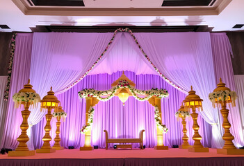  Temple-inspired wedding stage with golden lamp silhouettes, jasmine toran garlands, and pastel lavender curtain layers.