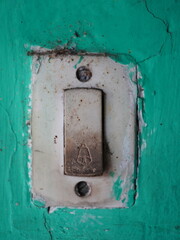 Grungy, weathered old doorbell button on vibrant teal cracked wall, evoking vintage charm.
