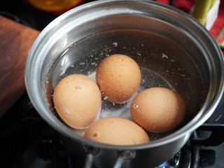 Four brown eggs gently boiling in a stainless steel pot filled with clear water