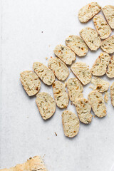 overhead view of slices of savory biscotti, top view of thinly sliced bread for making bread chips, top view of crostini bread slices on marble countertop