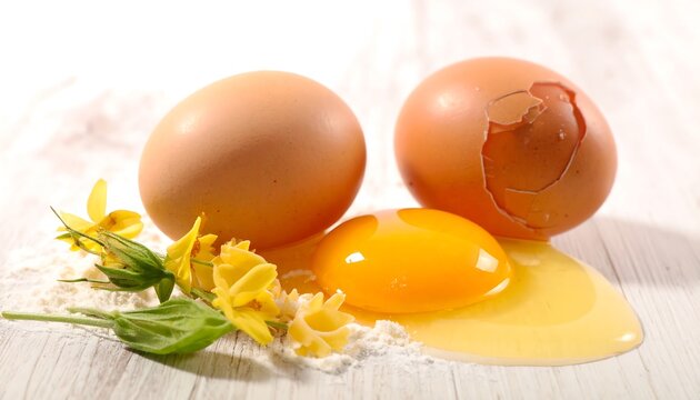 Fresh brown eggs and vibrant yellow yolk on a white wooden surface, accompanied by delicate yellow flowers. - Powered by Adobe