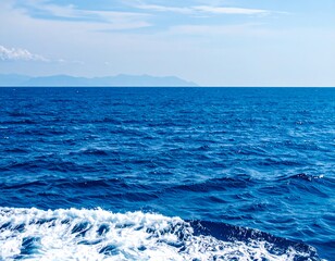 Wide expanse of deep blue ocean meeting a horizon of faint mountains under a partly cloudy sky