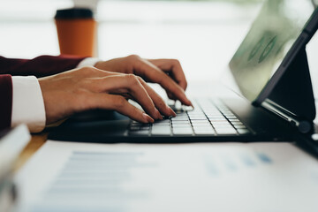 Fototapeta premium Business professional using tablet and laptop with financial charts and graphs on desk, analyzing business data and performance reports.