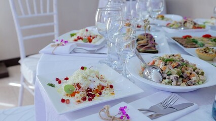 Gourmet salads artfully displayed on table, sprinkled with pomegranate seeds, fresh herbs, complemented by wine glasses, highlighting refined culinary presentation