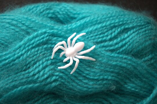 Close-up of a green yarn ball with a white plastic spider on top. Concept of life’s web, fate, and predestination.