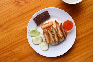 Exquisite Asian Cuisine: A top-down view captures the vibrant essence of an Asian dish, meticulously presented on a white plate, showcasing crispy pork, fragrant rice, cucumber slices, blood cake.