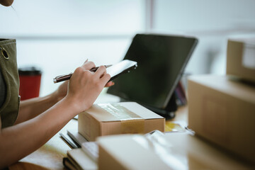 A young woman is packing a parcel with tape at a home office desk, surrounded by boxes, tablet, and coffee cup.