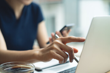Woman working on laptop computer and using smartphone at cafe. Asian casual business woman, freelancer remote working. Freelance, student studying online, e-learning