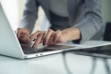 Closeup of businesswoman hand typing on laptop computer at office. Business woman working on computer, searching the information, surfing the internet on table at workplace