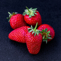 Bright red strawberries displayed on a dark surface create an appealing visual of ripe fruit ready for enjoyment or cooking