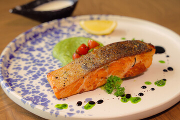 Gourmet Salmon Delight: A beautifully plated dish showcasing a perfectly cooked salmon fillet, complemented by vibrant green pea puree, fresh cherry tomatoes, and a zesty lemon wedge.