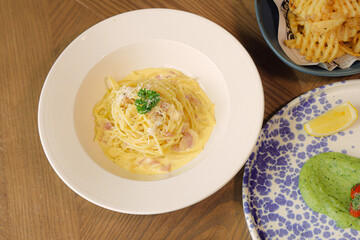 Exquisite Pasta Carbonara: An overhead shot showcases a classic pasta carbonara, garnished with fresh parsley. The scene is complete with crispy waffle fries and other culinary delights.