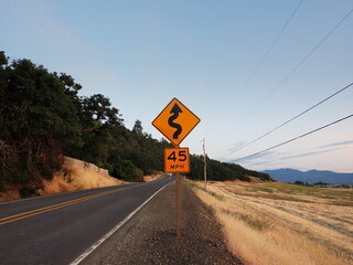 ASHLAND, OR, USA - June 14, 2025: A 45 MPH speed limit sign with curved road indicator with a rural...