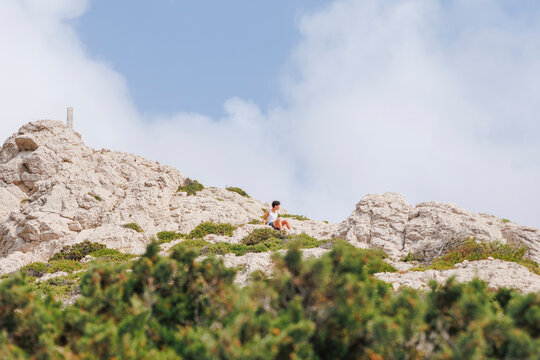 A teeny boy sits on rocky limestone peak against blue sky
