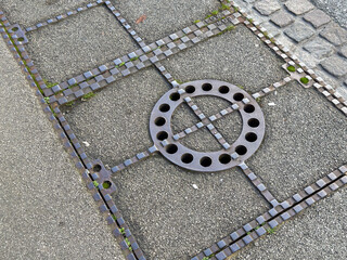 Metal grate on urban sidewalk with geometric design and cobblestone detail