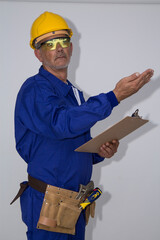 Repairman in a yellow hard hat and uniform holding a document. Handyman with a tool belt, isolated on white