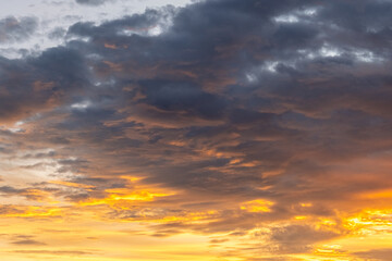 Dramatic sunset sky with golden and orange light illuminating dark clouds, creating a stunning natural background full of warmth, contrast, and atmospheric beauty.