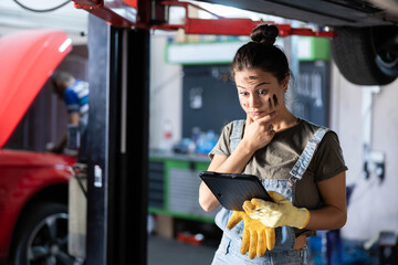 A thoughtful woman mechanic considers her next steps,using tablet, revealing insight and strategic thinking in the repair process.