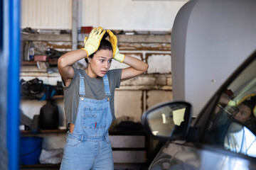 A distressed woman in a garage appears overwhelmed while working on her vehicle, showcasing the challenges of car maintenance.